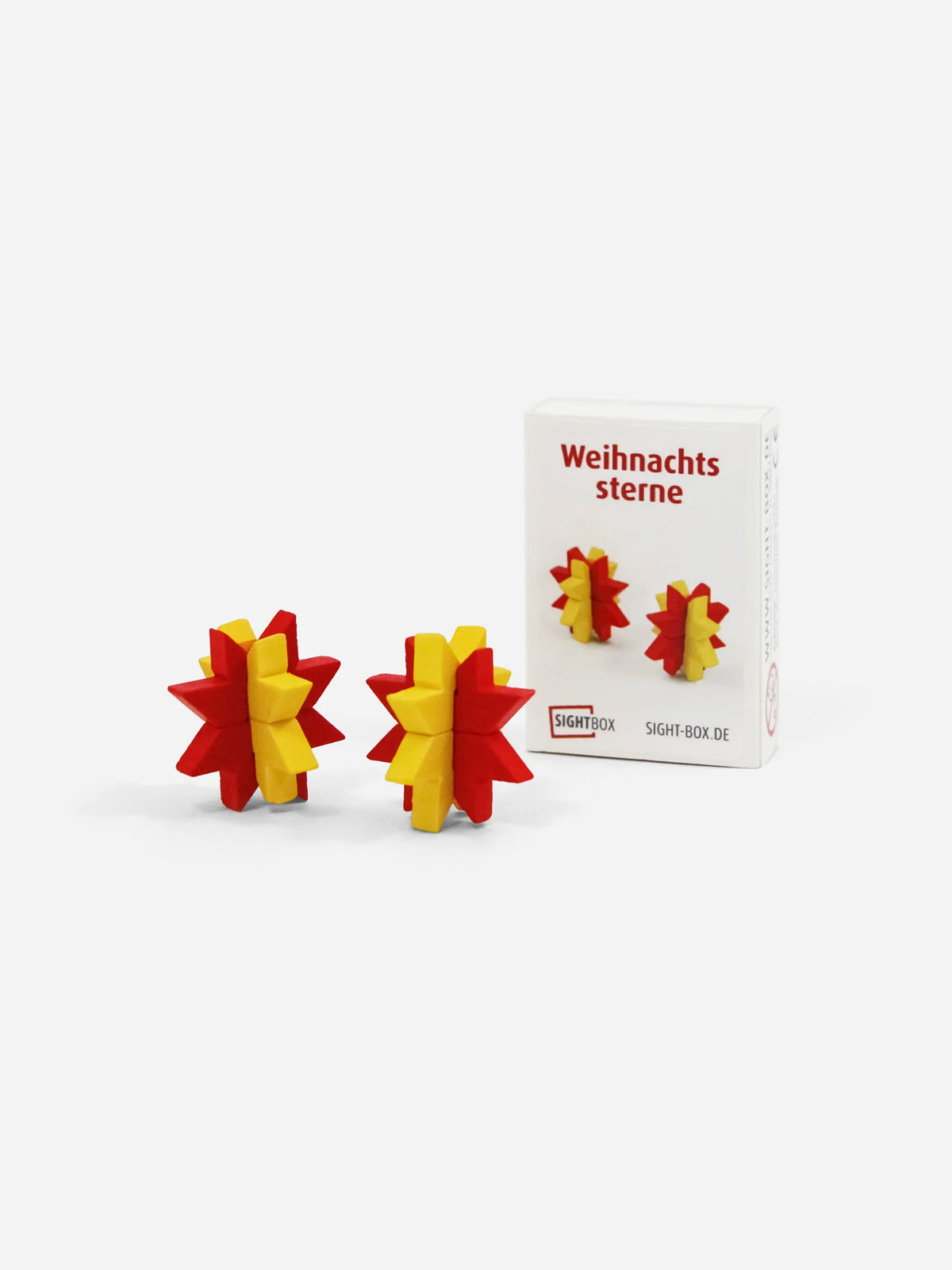 Holzbausatz Weihnachtssterne: zwei rot-gelbe Sterne aus Holz vor der weißen Sightbox-Schachtel mit Aufschrift „Weihnachtssterne“