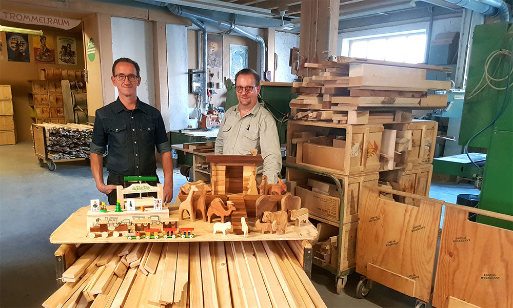Zwei Männer in der Holzwerkstatt von Loquai Holzkunst hinter einem Tisch mit Holzspielzeug und Holztieren